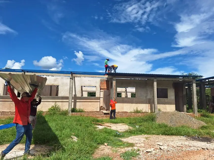 Workers install roofing on an unfinished building under a bright blue sky.